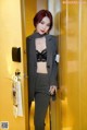 A woman in a black bra top and gray suit standing in an elevator.