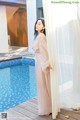 A woman standing next to a swimming pool wearing a long dress.