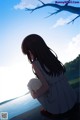 A girl in a white dress sitting on the edge of a lake.