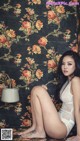 A woman sitting on the floor in front of a floral wallpaper.