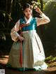 A woman in a green and white hanbok holding a flower.