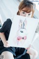 A woman sitting on the floor holding a painting of a rabbit.