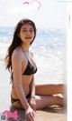 A woman in a black bikini sitting on the beach.